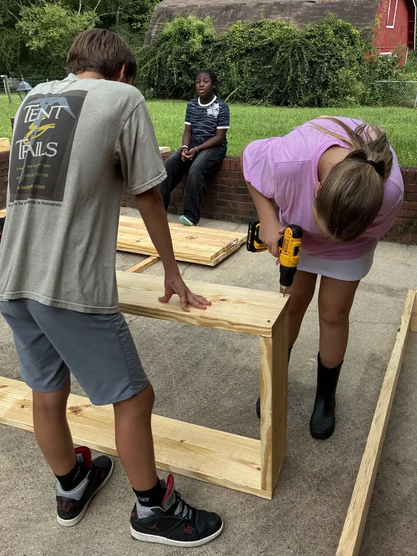 2 adolescent children using a drill to build a raised bed